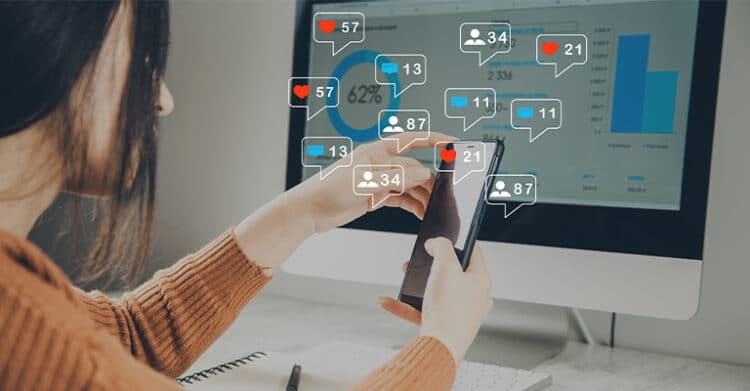 Person using a smartphone in front of a computer dashboard with floating social media notifications showing likes, comments, and follower counts. Visual for social media rules focused on managing engagement, tracking performance, and responding across platforms.