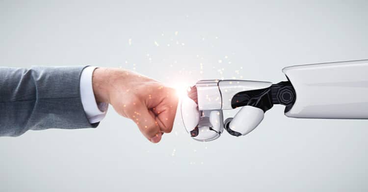 A human fist bumps a white robotic hand against a bright spark on a clean gray background. The visual represents human and AI collaboration in AI Content Strategy with technology supporting creative and strategic work.